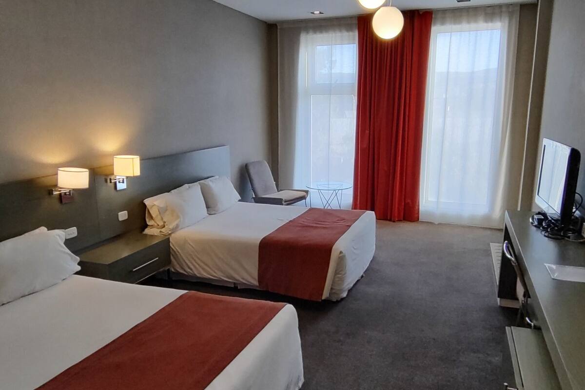 Habitació d'hotel amb dos llits, una taula de treball amb un ordinador, una cadira i una taula petita.