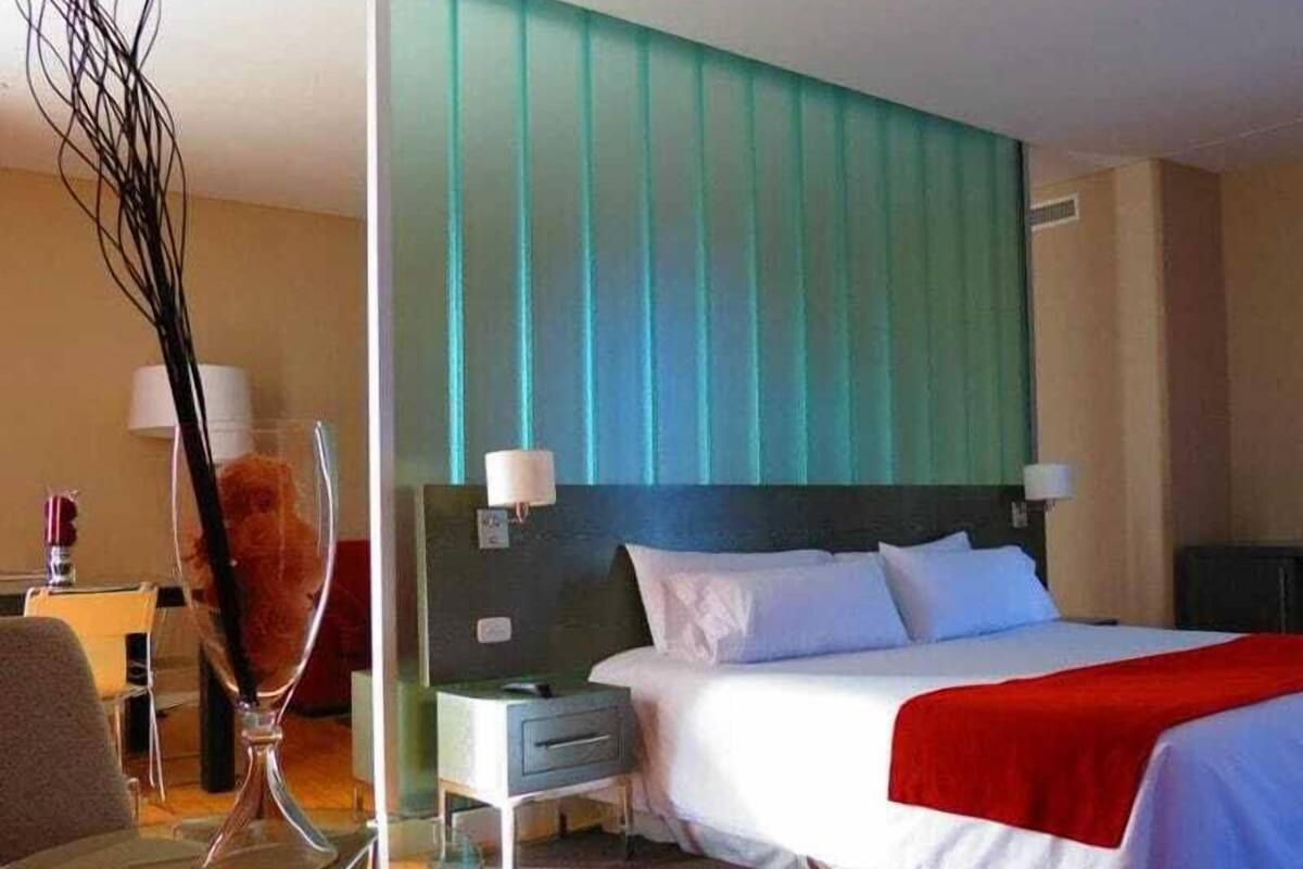Habitació d'hotel amb un llit gran, una nit, una cadira i un vas de vidre decoratiu.