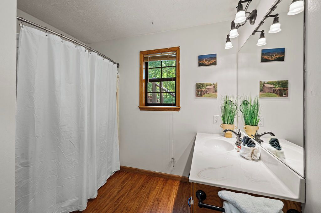 A bathroom with a shower curtain, a window, a sink with a mirror, and two potted plants.