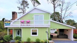 Una casa de dos pisos con fachada verde, un balcón con barandillas rosadas y un garaje.