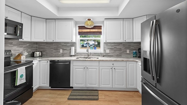 Una cocina moderna con armarios blancos, un refrigerador de acero inoxidable, un lavavajillas y un microondas.
