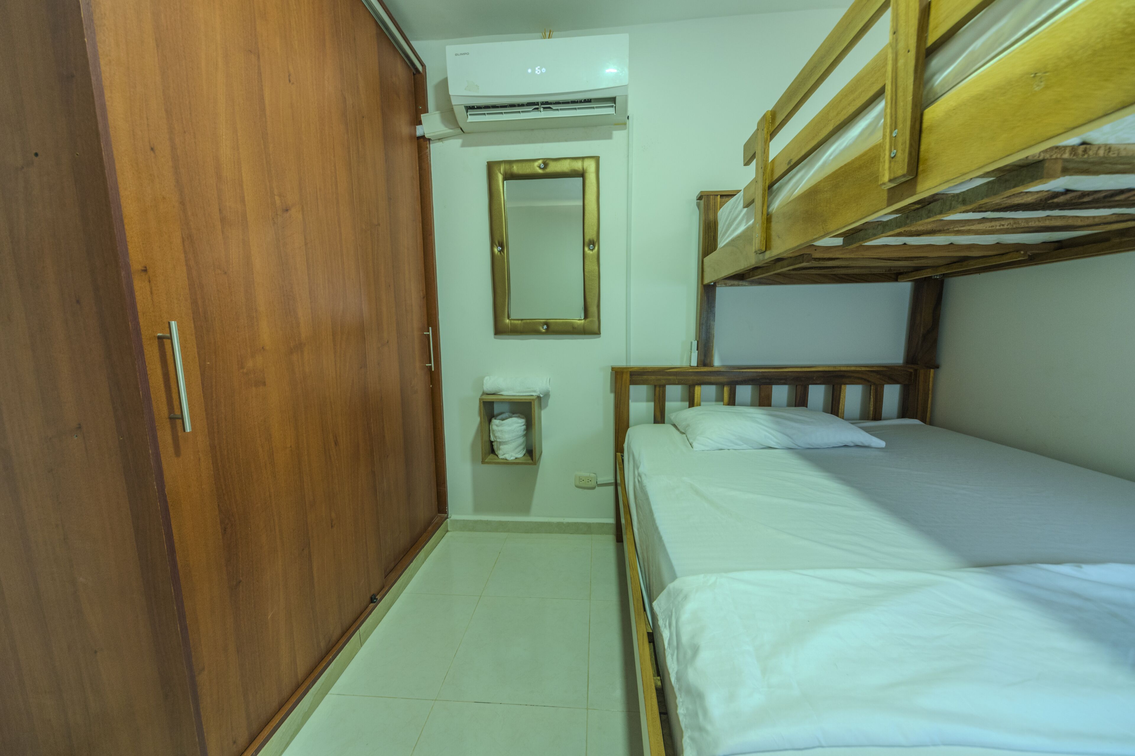 Une chambre avec un lit superposé, une armoire en bois, un miroir et un appareil de climatisation.