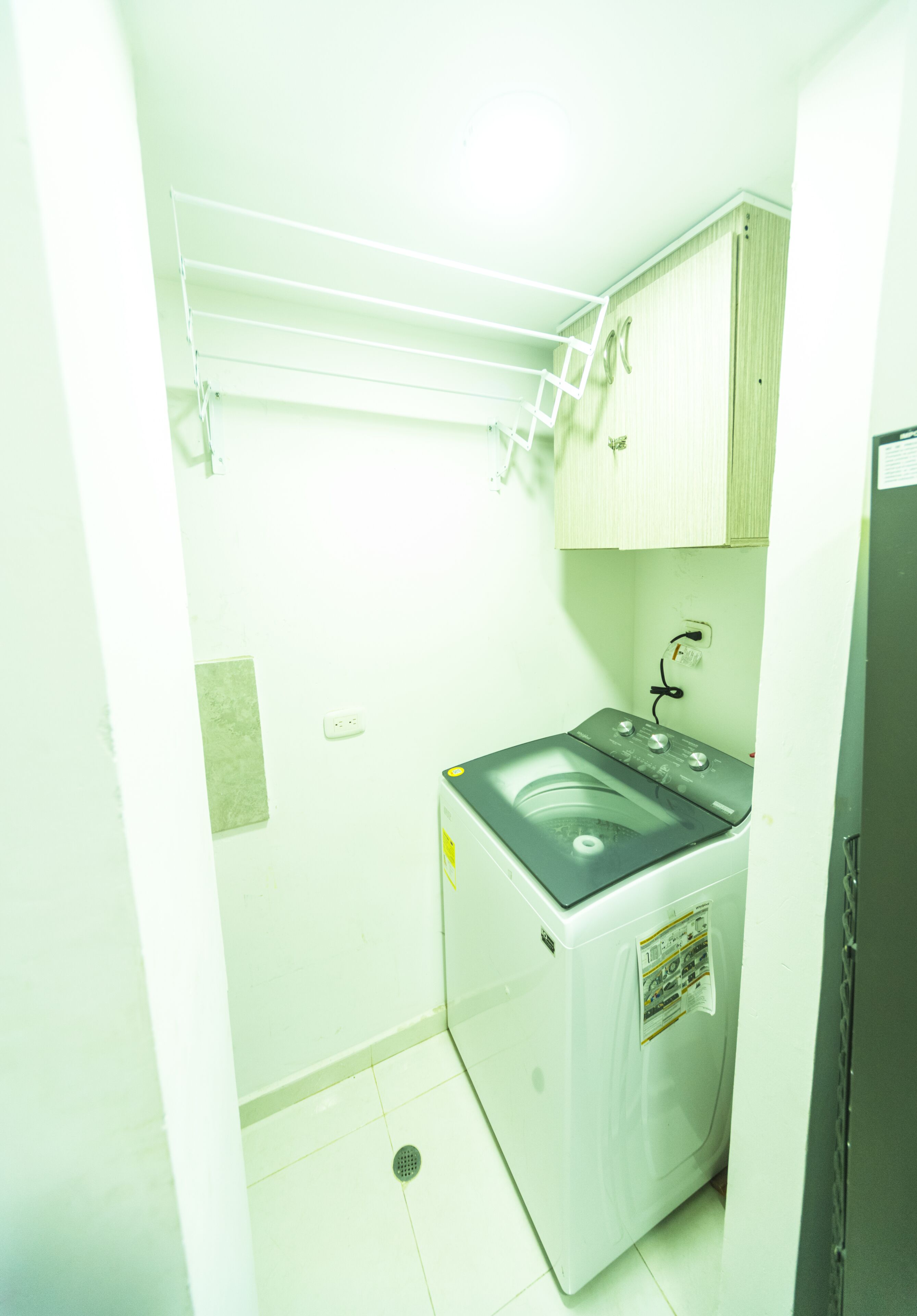 Une petite buanderie comprenant un lave-linge, un étendoir et un petit meuble de rangement.