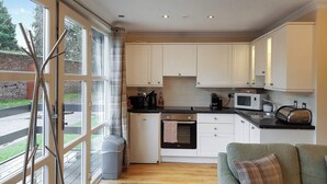 A modern kitchen with white cabinets, a black countertop, a microwave, and a toaster. There is a window with a view of a brick wall and greenery outside. - Leven Lodge 2 - UK46044 (Loch Lomond)
