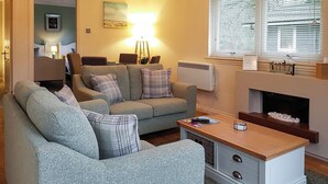 A living room with a sofa set, a coffee table, a fireplace, and a window with blinds. - Leven Lodge 2 - UK46044 (Loch Lomond)