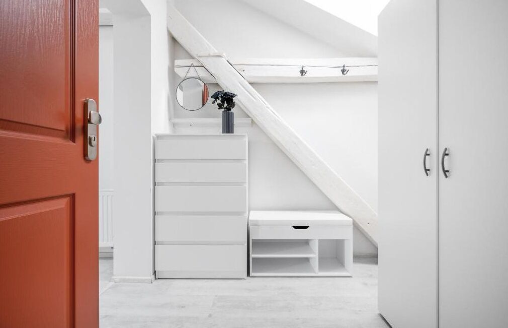 Ein Zimmer mit einem weißen Kleiderschrank, einer roten Tür, einer weißen Kommode und einer weißen Bank.