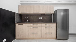 Eine moderne Küche mit hellen Holzschränken, einem Edelstahlkühlschrank und einer schwarzen Arbeitsplatte.