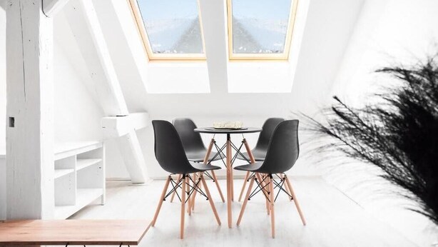 Ein moderner Essbereich mit einem runden Tisch, vier schwarzen Stühlen, einer weißen Bank und einem großen Fenster mit Blick auf eine verschneite Landschaft.