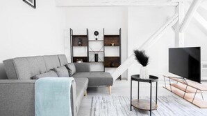 Ein modernes Wohnzimmer mit einem grauen Ecksofa, einem schwarzen TV-Schrank und einer Holztreppe.