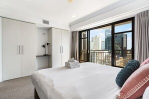 A hotel room with a large bed, a wardrobe, a desk, and a view of the cityscape.