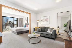 Una habitación de hotel moderna con cama, sofá, mesa de centro redonda y un espejo grande.