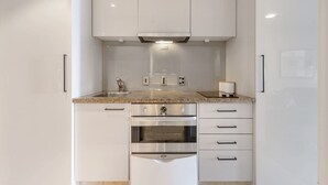 A compact kitchen with white cabinets, a stainless steel oven, and a granite countertop. - Stunning City Views - w Pool&Gym (Auckland)