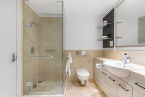 Un baño moderno con cabina de ducha de vidrio, inodoro blanco y tocador con lavabo y espejo.