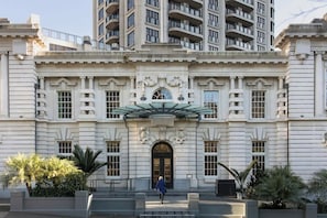 Un edificio grande de estilo clásico con una entrada central, varias ventanas y una persona caminando hacia ella.