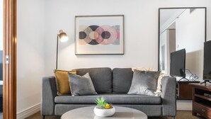A living room with a grey sofa, a round coffee table with a plant, a floor lamp, and a framed abstract painting on the wall. - Stunning City Views - w Pool&Gym (Auckland)