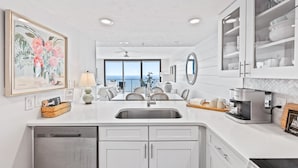 A modern kitchen with a dishwasher, a coffee maker, and a dining area with a view.