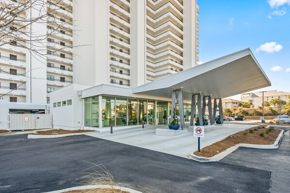 A modern building with a covered entrance, large windows, and a parking area.