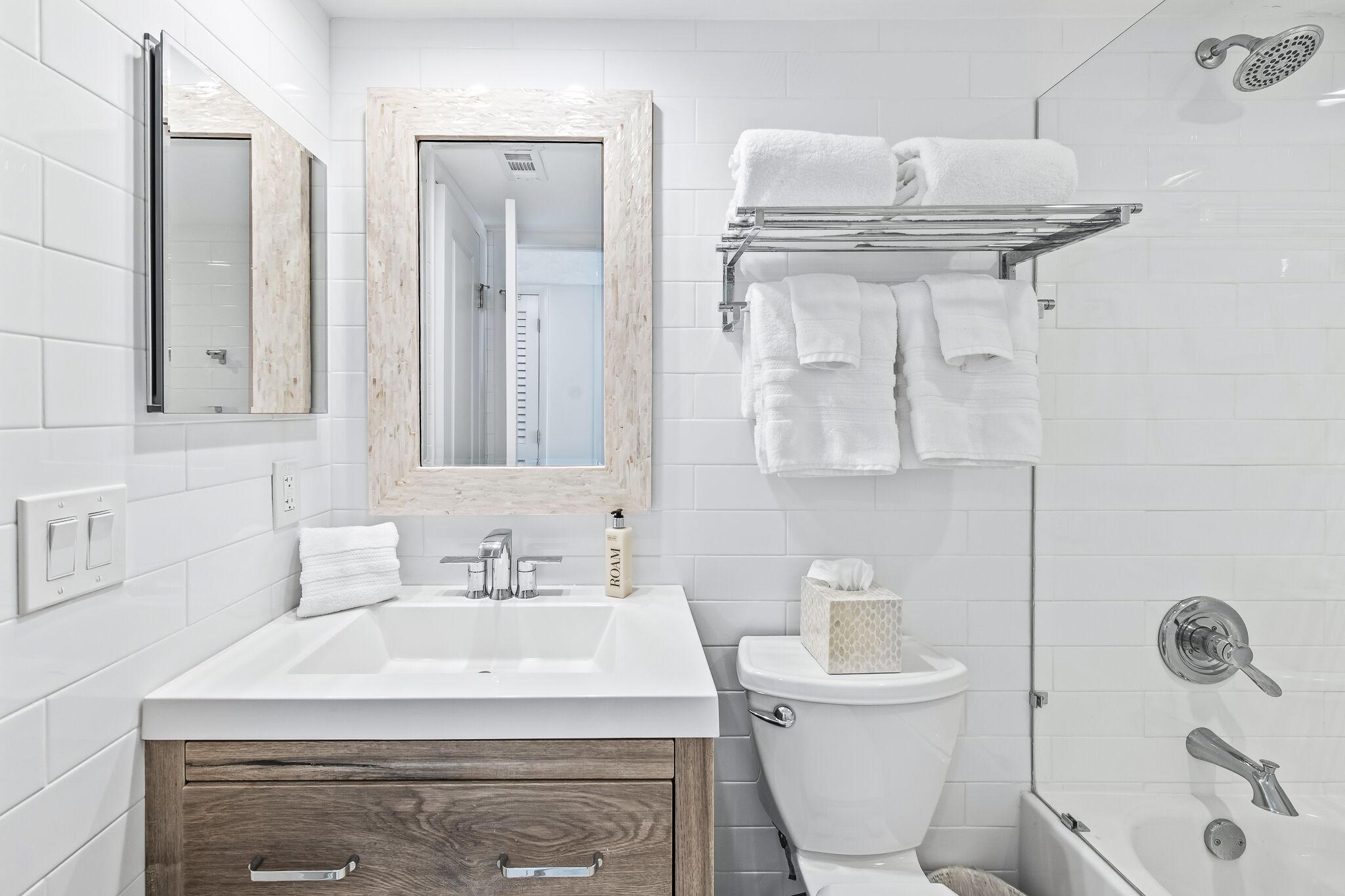A modern bathroom with a white sink, mirror, and toilet. There is a towel rack with towels and a showerhead.