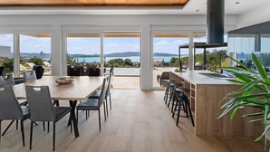 Une cuisine moderne dotée d’un grand îlot central, d’un coin repas offrant une vue agréable et d’une vaste terrasse avec espace salon extérieur.