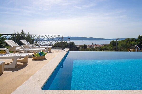Una piscina con sillones de descanso y vistas al mar.