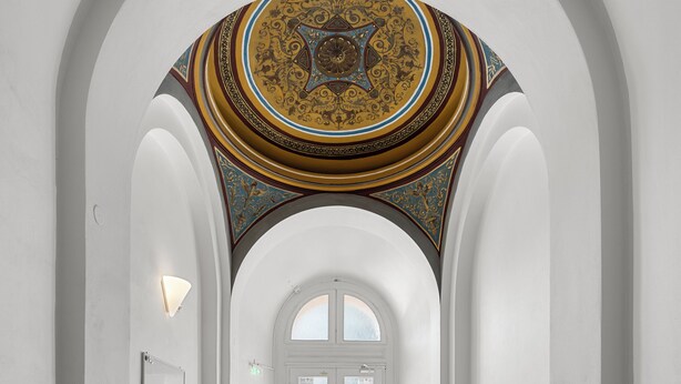 Ein Korridor mit Holzboden, weißen Wänden und einer verzierten Decke.
