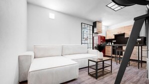 Ein modernes Wohnzimmer mit einem weißen Sofa, einem kleinen Couchtisch und einer Küchenzeile im Hintergrund.