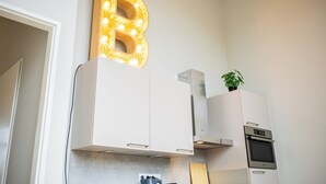 A modern kitchen with white cabinetry, a built-in oven, and a decorative illuminated letter 'B' on the wall.