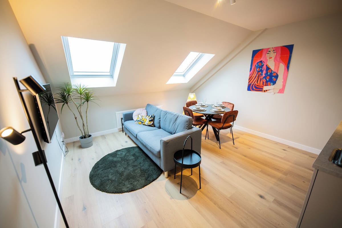 A modern loft apartment with a dining area, a sofa, a small table, and a painting on the wall.