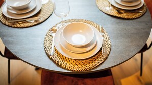 A round table with a woven placemat, a white bowl, a wine glass, and a fork.