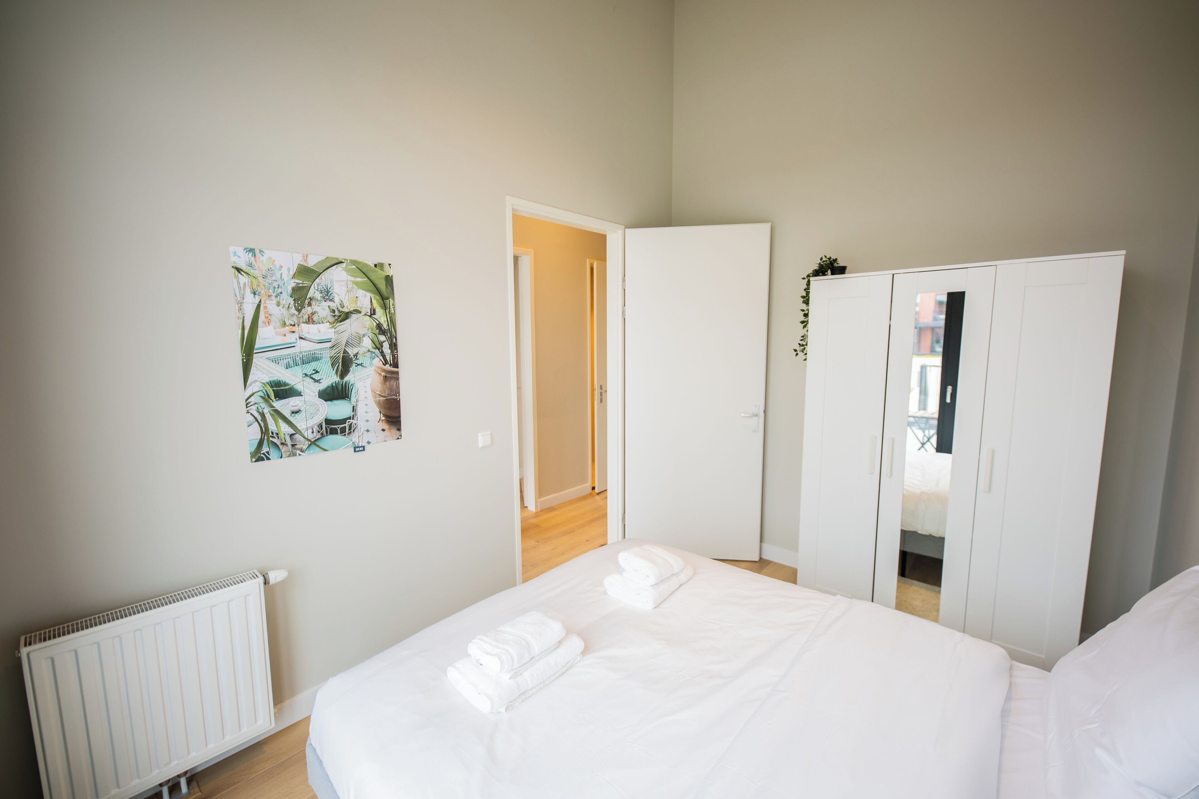 A bedroom with a bed, a radiator, a wardrobe, and a door leading to another room.
