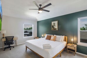 Un dormitorio con cama, escritorio, silla, ventilador de techo y ventana con vistas.
