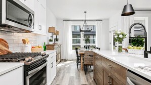 A modern kitchen with white cabinetry, a central island, and a dining area with a view of the outside. - Meridian Marvel Luxury Home (Meridian)