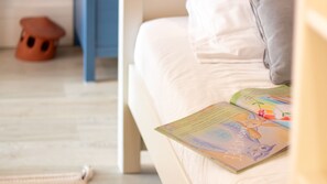 Un lit avec un livre dessus, une chaise bleue et un petit tabouret orange.