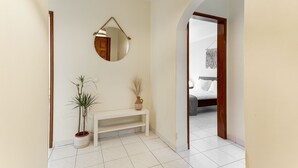 Un pasillo con un banco blanco, una planta en maceta, un espejo y una puerta que da a un dormitorio.