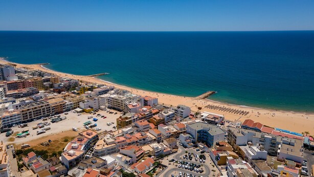Vista aérea de un pueblo costero con playa, edificios y un cielo azul despejado.