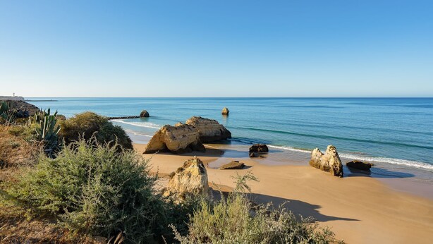 A coastal landscape with large boulders, a sandy beach, and sparse vegetation. - Praia da Rocha Wonder w/ Balcony by LovelyStay (Praia da Rocha)