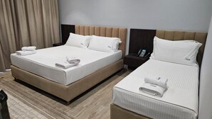 A hotel room with two beds, each with a headboard, a bedside table with a phone, and a rolled towel on the bed. - KAAN Hotel (Orikum)
