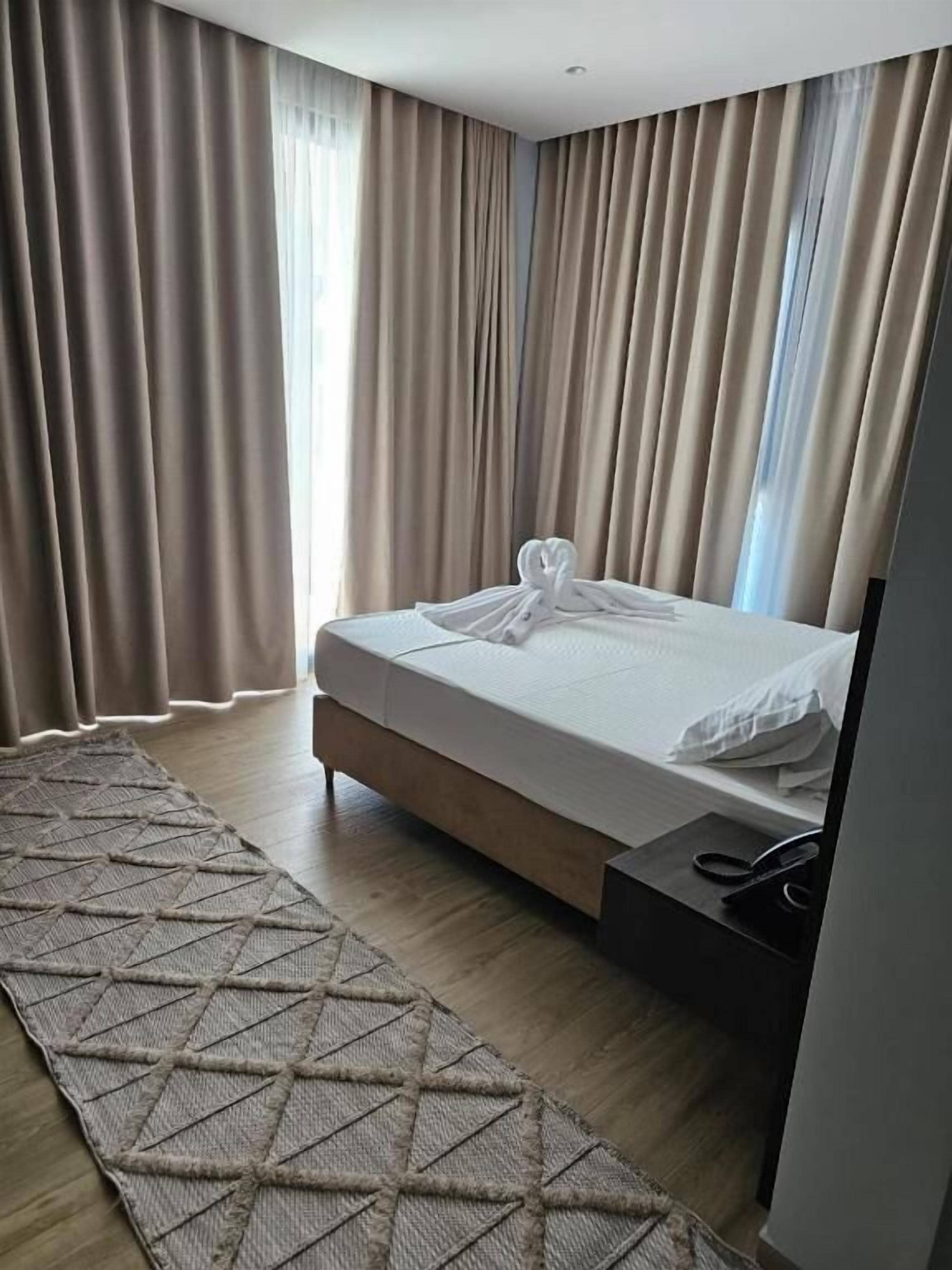A hotel room with a bed, curtains, a rug, and a nightstand.