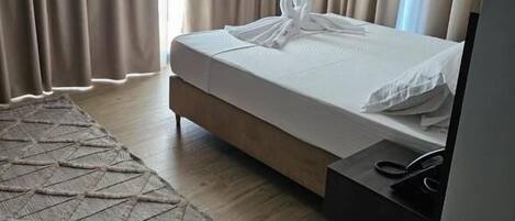 A hotel room with a bed, curtains, a rug, and a nightstand.