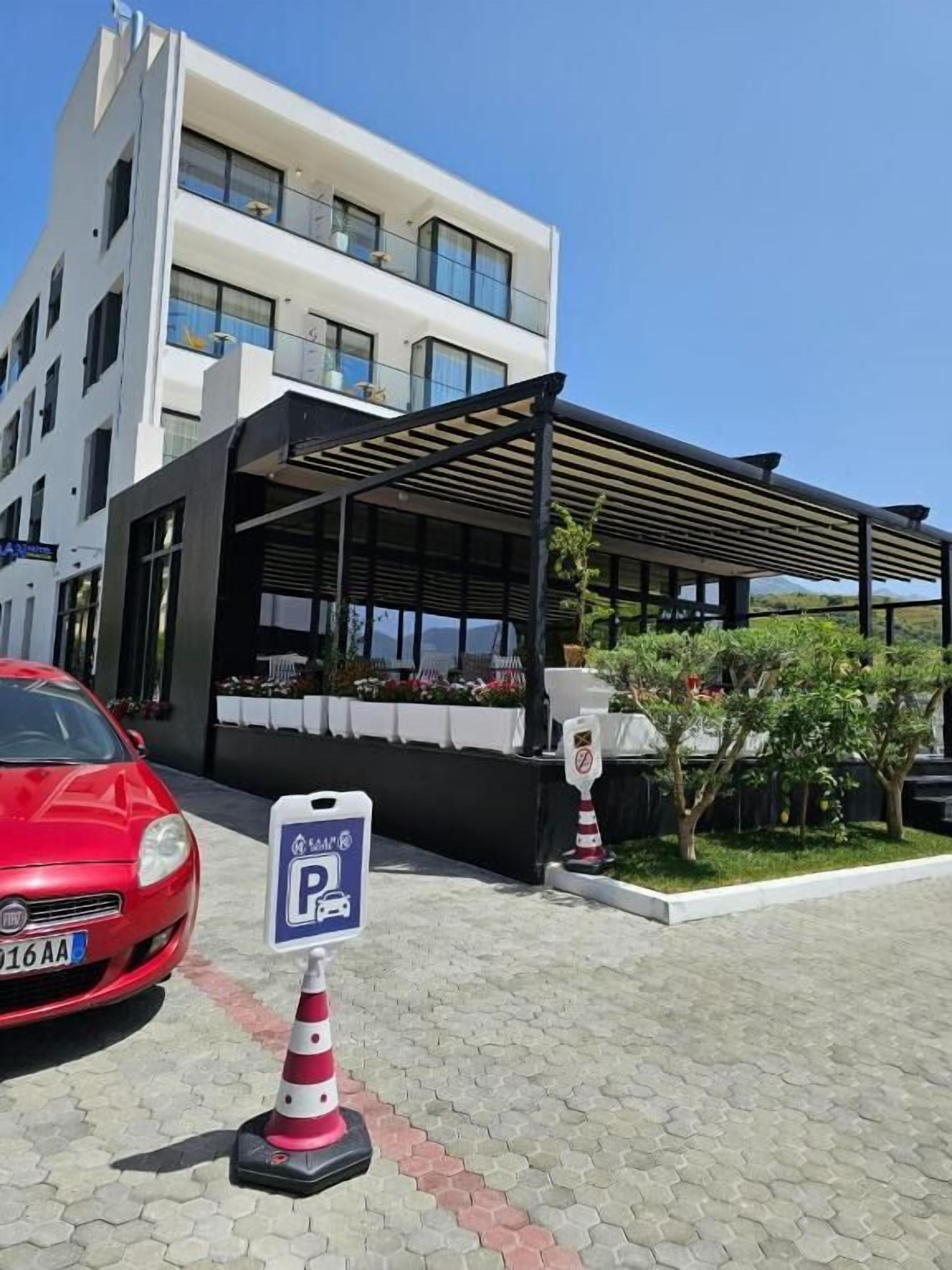 Un bâtiment moderne doté d’un espace extérieur couvert, d’un panneau indiquant l’emplacement du parking et d’une voiture rouge garée devant.