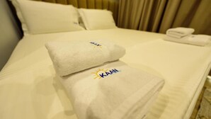 A neatly made bed with a white bedspread and two pillows. A towel with the logo "KAAN" is placed on the bed. - KAAN Hotel (Orikum)