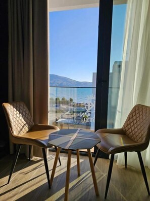A modern room with two leather chairs and a small table, large windows with a view of a body of water and buildings, and a patterned carpet. - KAAN Hotel (Orikum)