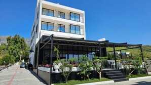 A modern two-story building with a covered outdoor area, a car parked in front, and a clear blue sky. - KAAN Hotel (Orikum)