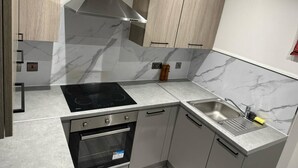 Una cocina moderna con estufa, horno y pileta integrados, alacenas de madera clara y salpicadero de mármol.