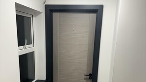 Un pasillo con una puerta de madera, un ventanal pequeño y una estantería.