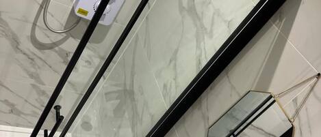 A bathroom with a glass-enclosed shower, a white sink, and a marble floor.