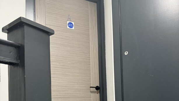 Una puerta de madera con un letrero que indica 'mantener puerta cerrada en caso de incendio', un marco de puerta negro y una escalera con barandilla negra.