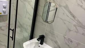 Un baño con ducha de vidrio, un lavabo blanco con grifo negro y un inodoro.