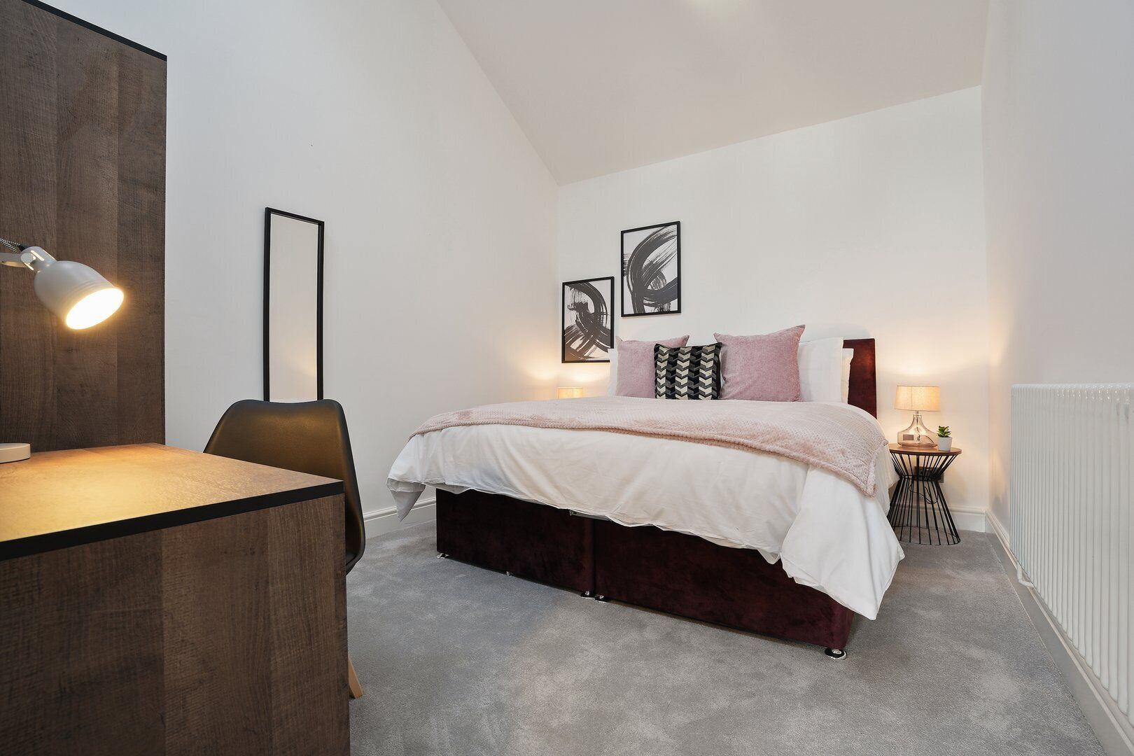 Een slaapkamer met een bed, nachtkastje, lamp en stoel.