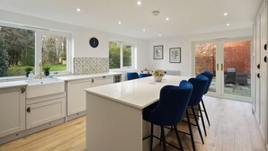 A modern kitchen with a central island, bar stools, and a view of a brick wall and garden through a glass door.